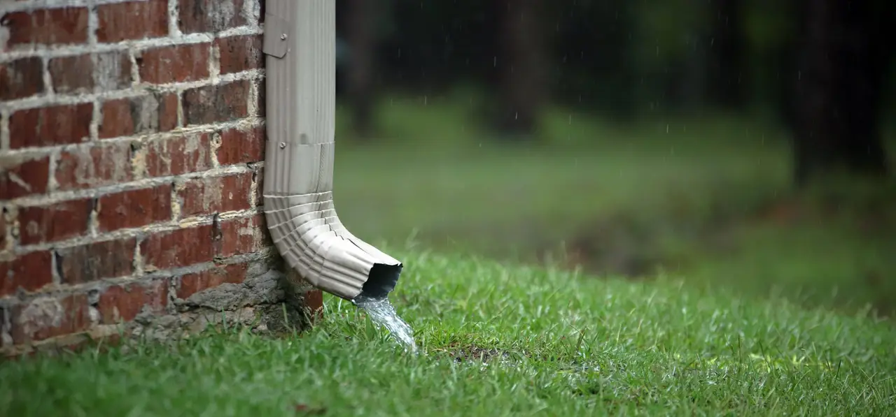 Aluminum downspout running down a brick wall and discharging onto grass