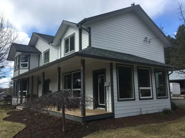 Grey and white farmhouse-style home in the Cariboo with a wraparound porch and finished gutters