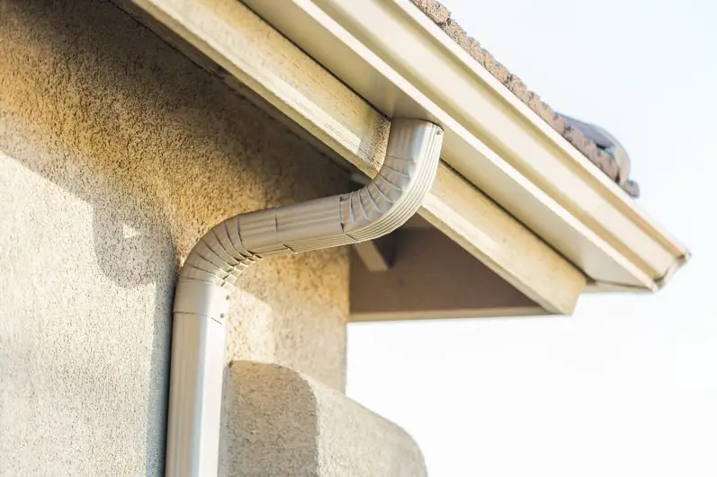 Gutter and downspout outlet installed on a stucco wall